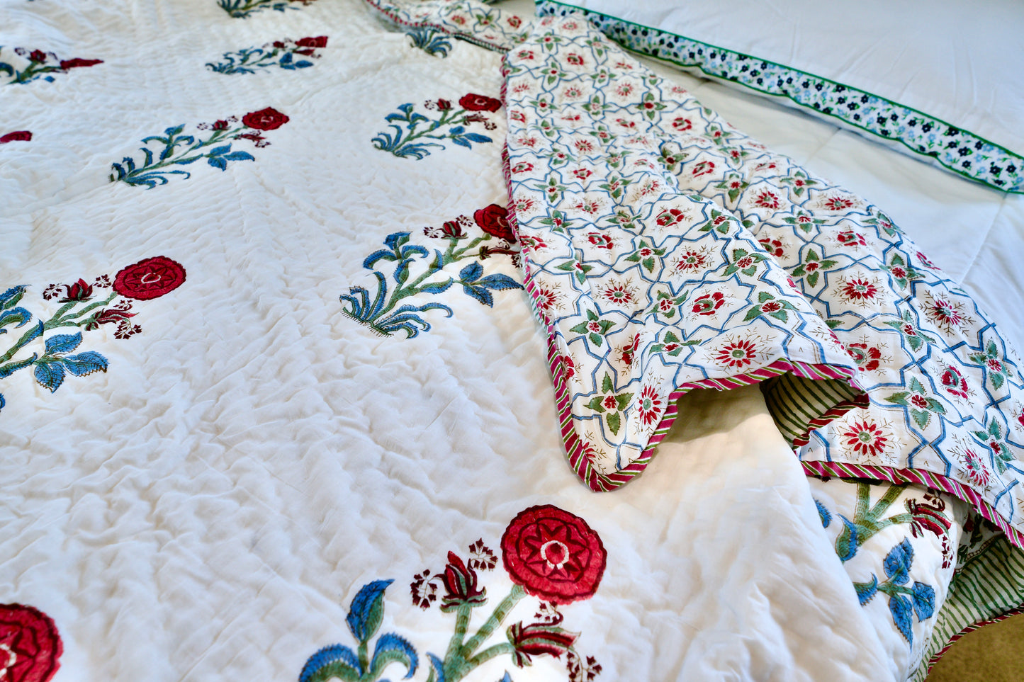 Reversible Harmony organic cotton quilt, hand block printed with red florals and green-blue leaves on one side, and a trellis pattern with red blossoms and green vines on the reverse
