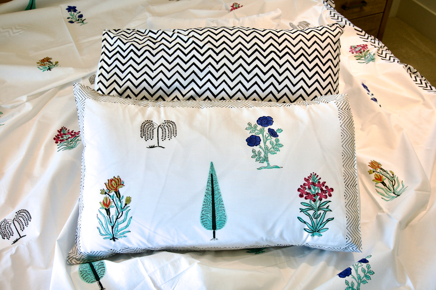 Two pillows on a bed with one featuring floral embroidery and the other with a chevron pattern.