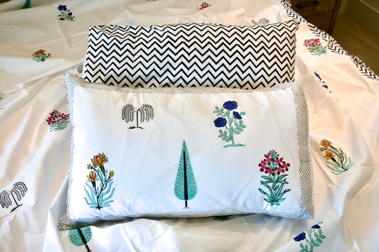 Two pillows on a bed with one featuring floral embroidery and the other with a chevron pattern.