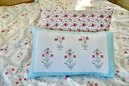 Coral Veil hand block printed organic cotton bedsheet with coral-pink floral motifs, green stems, white base, light blue pillow border, and matching vine-patterned pillowcases.