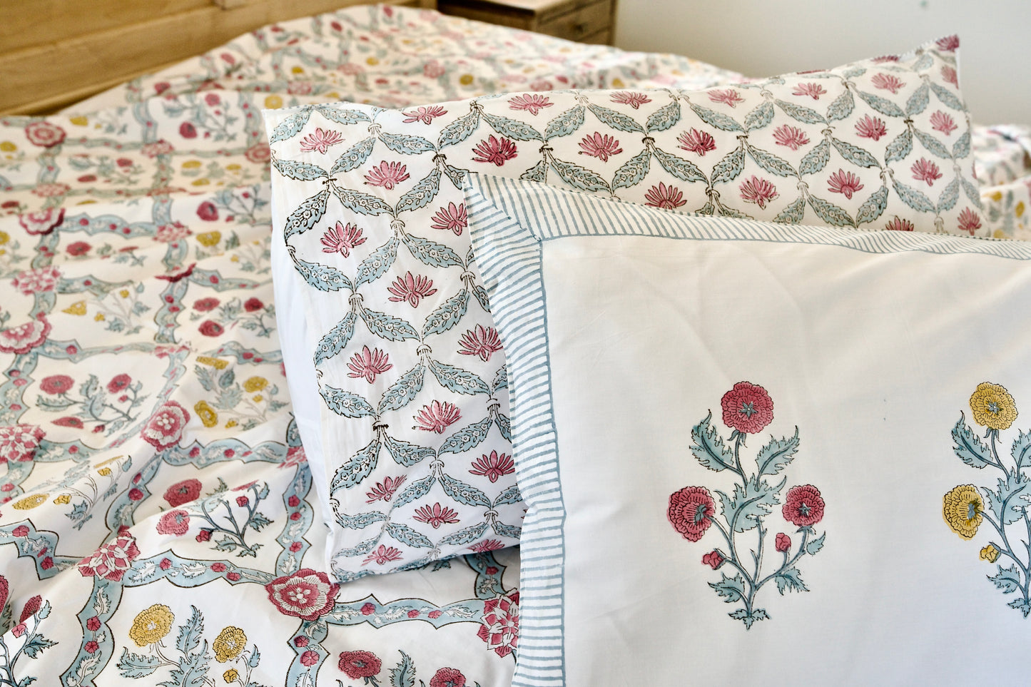 Floral Tapestry hand block printed organic cotton bedsheet with red, yellow, and pink floral motifs, green leaves, white base, striped pillow border, and vine-patterned pillowcases