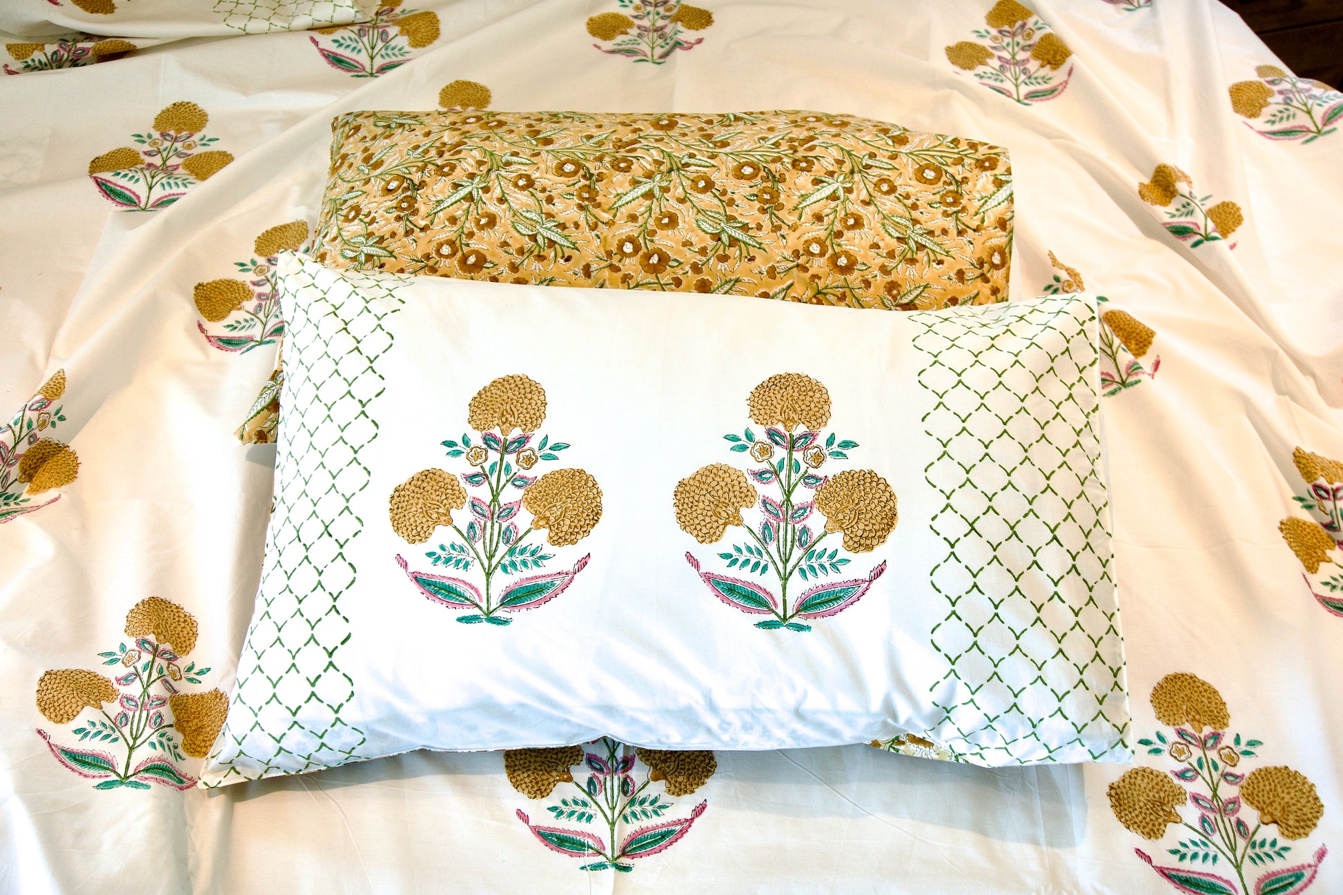 Golden_Marigold Hand block printed organic cotton bedsheet with golden-yellow floral motifs, green lattice detailing, pink accents, and matching pillowcases with yellow floral repeat patterns