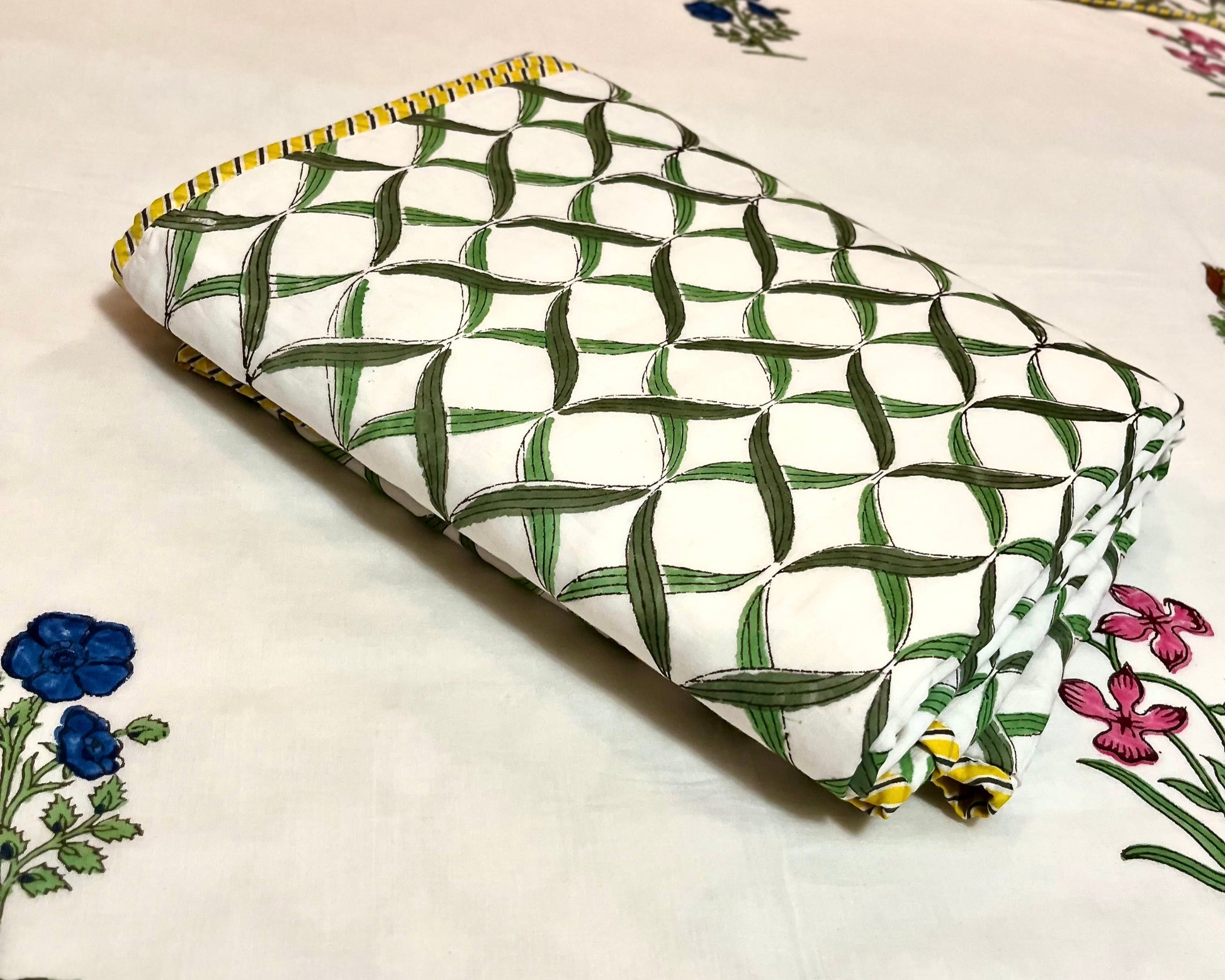 Green and white patterned pouch on a floral bedspread