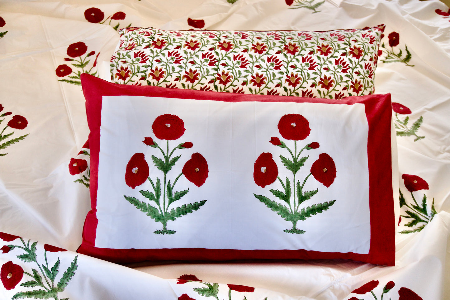 Rosewood Royale hand block printed organic cotton bedsheet with bold red floral motifs, green leaves, white base, and red border pillowcases.