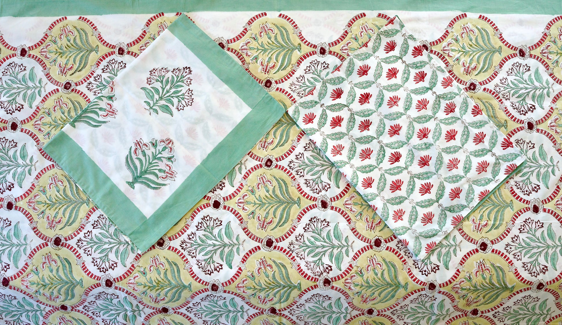 Verdant Arch hand block printed organic cotton bedsheet with green leafy motifs framed in golden arches with red accents on a white base, paired with green-bordered and vine-patterned pillowcases